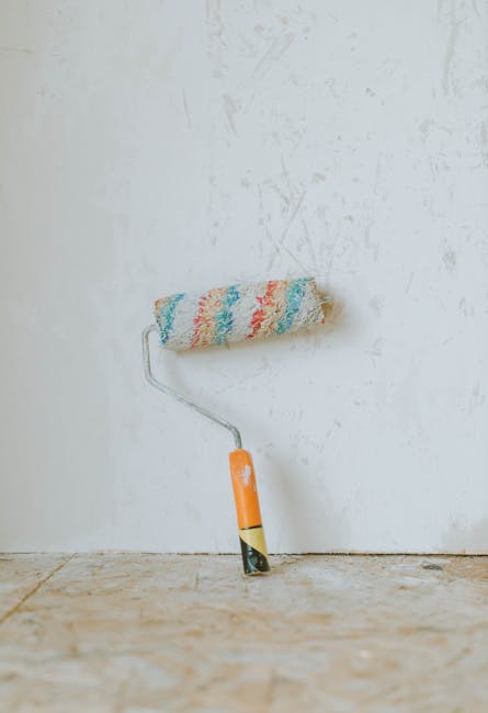 A vivid paint roller rests against a textured white wall on a wooden floor, perfect for renovation themes.